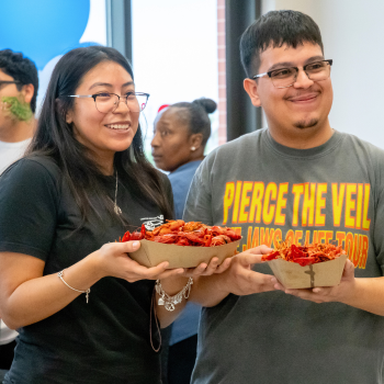Two University of Houston-Downtown students smile while holding containers of crawfish at UHD's Bayou Bash in the food court area.