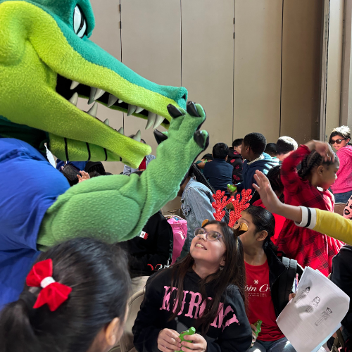 students at Houston ISD's Dogan Elementary wave and smile at University of Houston Downtown's mascot Ed-U-Gator 