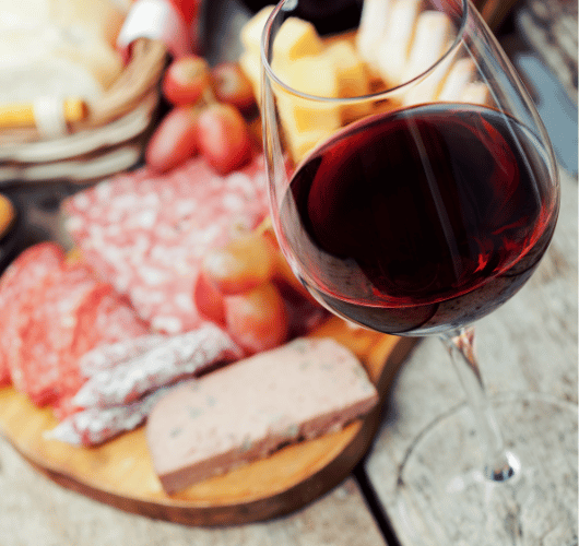 glass of beaujolais and a serving board with meats, cheese, and fruits